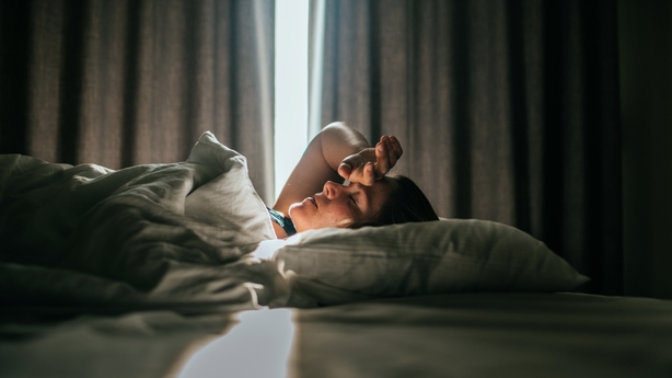 Woman awaking after sleeping well in a nice sleeping room.. Sunny daylight is coming through the curtains in the back.She had one hand on her forehead.