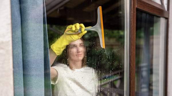 A woman cleaning window glass of country house with a squeegee. Photographed through window