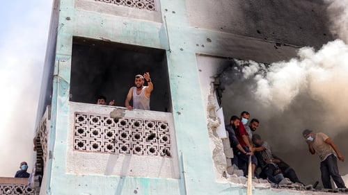 A man shouts out to others below while first-responders attempt to extinguish a blaze in western Jabalia