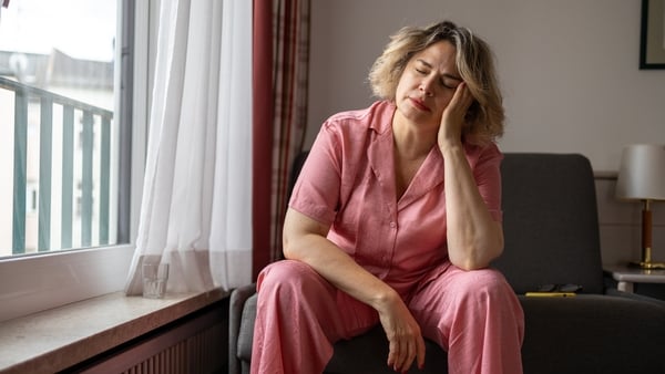 Mature woman suffering from a headache and holding her head with hands while sitting on sofa at home. Menopause and depression. Mental health concept