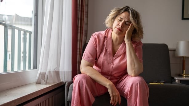 Mature woman suffering from a headache and holding her head with hands while sitting on sofa at home. Menopause and depression. Mental health concept