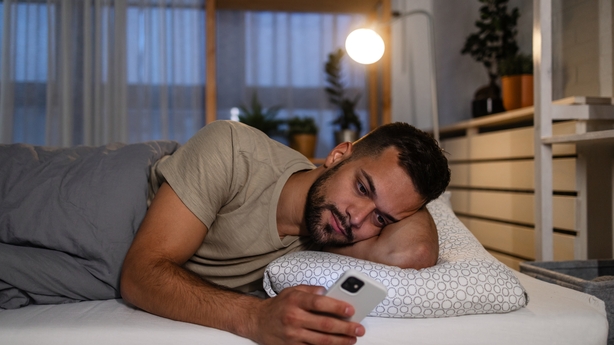 A sleepy man using a phone in the bed. He is trying to fall asleep.