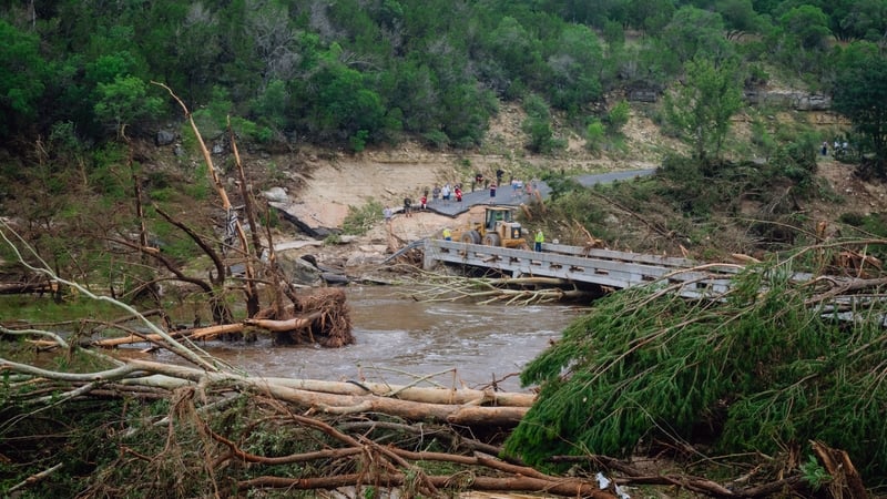 Construction crews clears debris for residents to cross a bridge over the Guadalupe River in Ingram, Texas