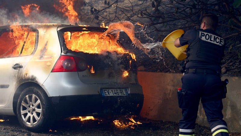 A police officer tries to put off the fire in a car during a wildfire in the L'Estaque district of Marseille