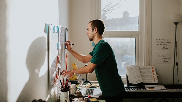A man in a sunny home office writes on a white board with a marker.