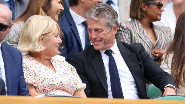 Hugh Grant interacts with guests in the Royal Box prior to the Ladies' Singles quarter-final match between Mirra Andreeva and Belinda Bencic of Switzerland on day ten of The Championships Wimbledon 2025 at All England Lawn Tennis and Croquet Club on July