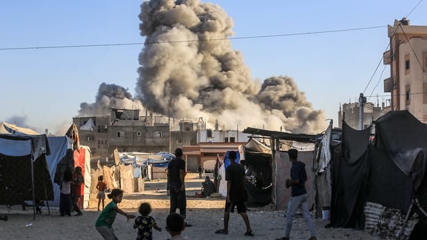 a group of people in Khan Younis with a cloud of smoke in background