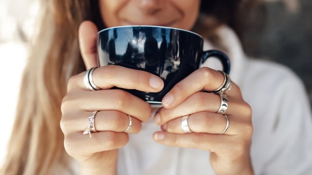 Closeup hand of woman holding a coffee cup and wearing silver rings