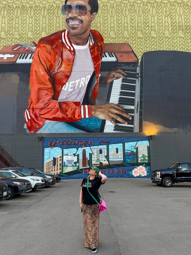 a person standing in front of a mural of a person with the sign 'Detroit'