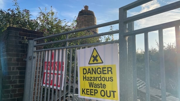 A sign reads 'danger, hazardous waste', with a view of a controversial Belfast bonfire in the background