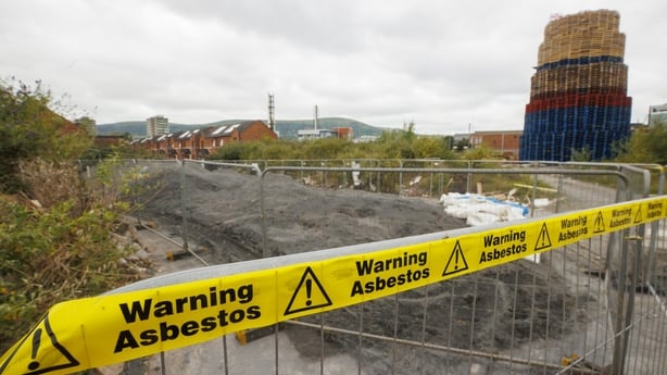 A controversial bonfire in Belfast is seen in the background, with yellow tape reading 'warning, asbestos' in front of it