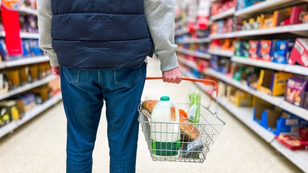 Low angle close up colour image depicting a man holding a shopping basked filled with fresh groceries