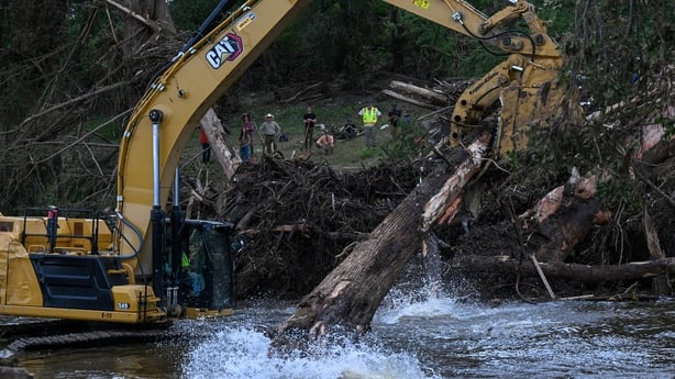 Volunteers watch as an excavator removes trees damaged in the Central Texas floods