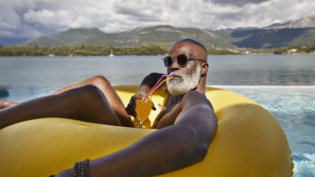 Bald senior man wearing sunglasses while drinking juice in inflatable ring during vacation