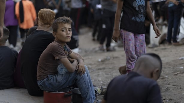 A Palestinian child holds an empty pot while waiting to receive food distributed by a charity in the Al-Rimal neighbourhood of Gaza City