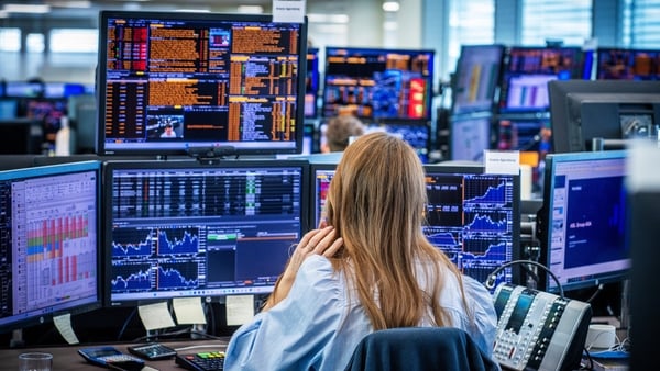 Female stock trader on front of a rake of computer screens showing financial market data