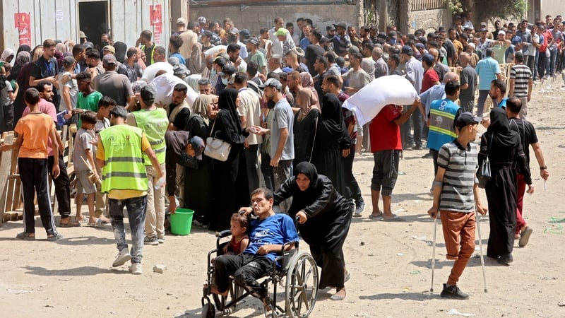 A Palestinian woman pushes a man and child on a wheelchair as people gather to receive bags of flour at a WFP warehouse in Gaza city