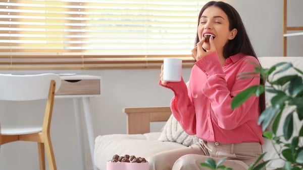 a woman sitting on a couch eating a cup of coffee and eating chocolate