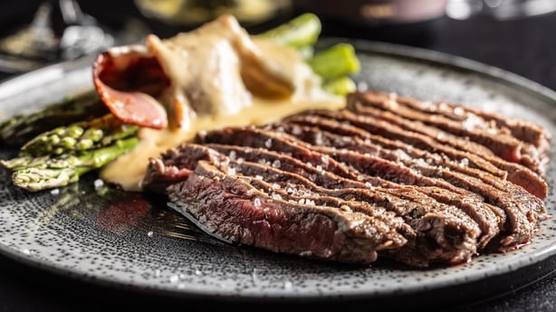Juicy beef flank steak with asparagus and bacon covered in hollandaise sauce. Bottles with wine and glasses in the background.