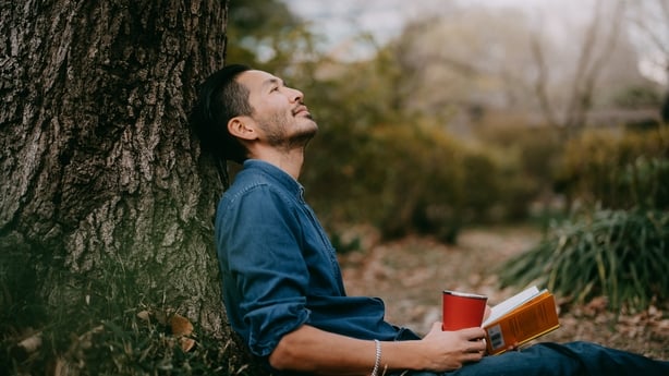 Japanese man relaxing with book and coffee in park