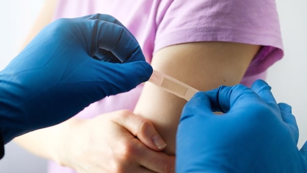 A gloved doctor or health care professional applies a patch or adhesive bandage to a girl