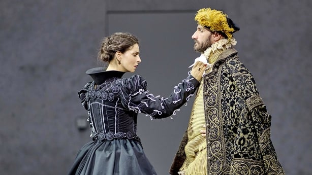 A woman in a blue dress and a man in a gold renaissance jacket speak