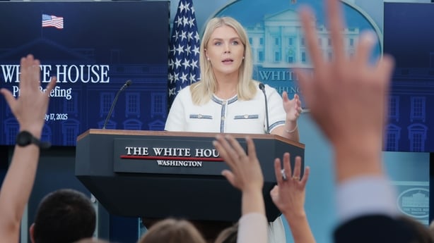 Karoline Leavitt standing at a podium with a crowd of people raising their hands