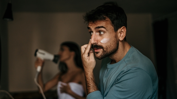 The man moisturizes his skin while the woman skillfully blow-dries her hair