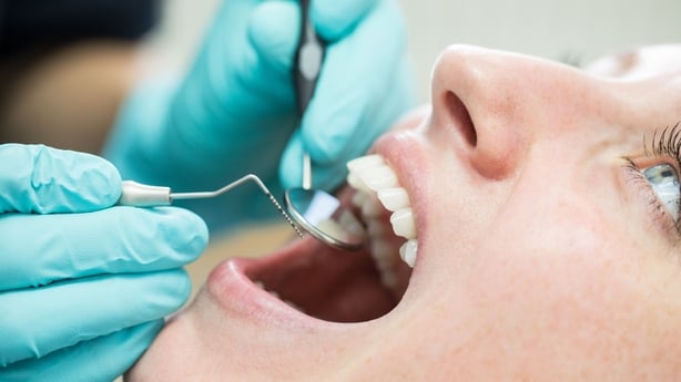 Close up of dentist holding angled mirror and hook while examining patient. 