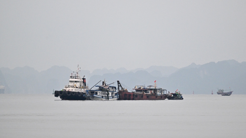 The tourist boat (C) that capsized is towed back to the port in Ha Long bay, Quang Ninh province