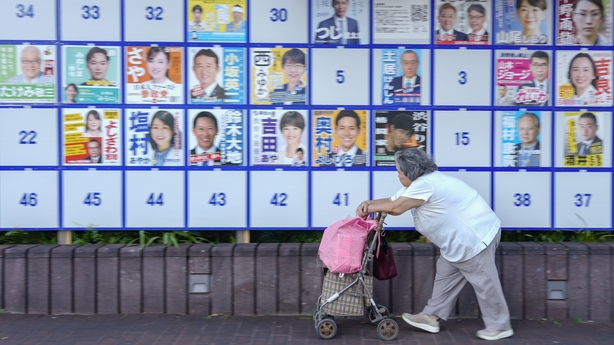 A woman walks in front of an election notice board displaying posters of candidates in Japan's election in Tokyo, Japan, on Sunday, July 20, 2025