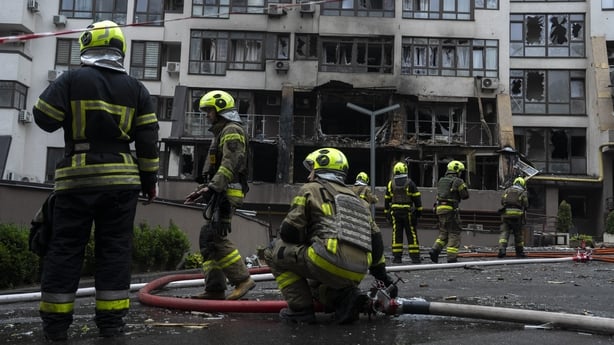 Firefighters stand near a damaged building following a Russian attack in Kyiv