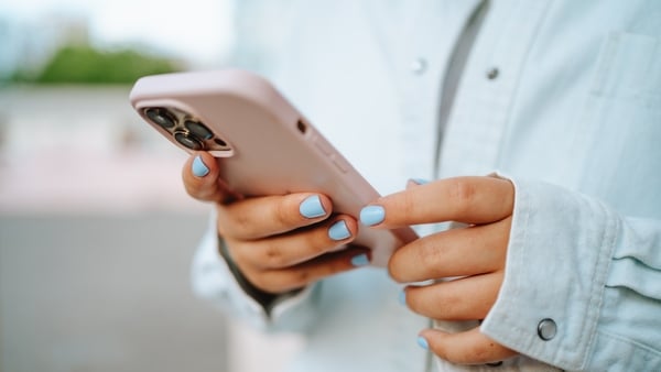 A woman wearing her a denim shirt holds her smart phone in her hand