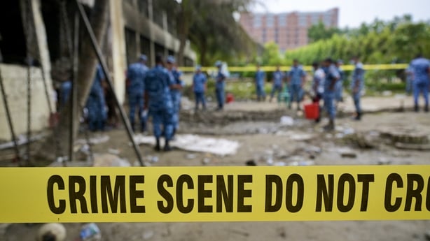 A crime scene barrier tape cordons off the area as Bangladesh Air Force personnel inspect the crash site
