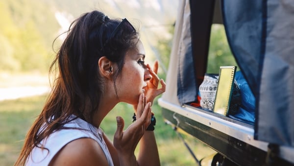 Young woman putting makeup or just washing her face in the morning in front of her rooftop tent during camping in the nature.