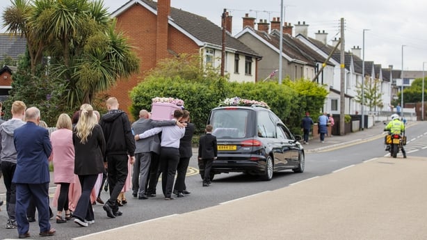 a group of people walking down a street with a car carrying a box