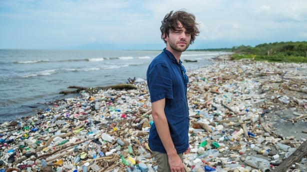 a person standing in front of a pile of plastic waste floating on the shore