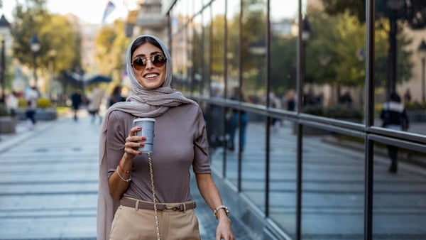 Smiling Muslim woman wearing hijab headscarf walking in the city center. Arab female in urban background