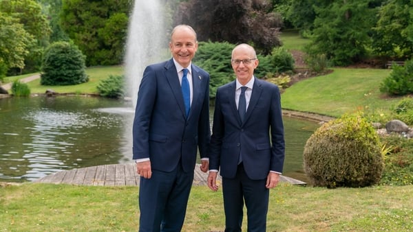 two men in suits standing in front of a fountain