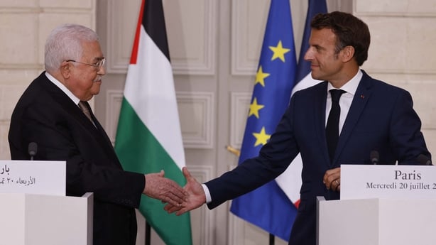 Two men shaking hands with the French flag and Palestinian flag seen in the background on a stage