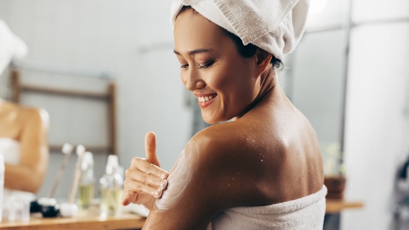 Young Asian woman following her skin care routine, she is applying the cream after a shower.