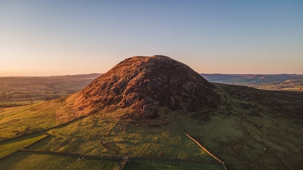 Aerial drone view of Slemish mountain near Ballymena, County Antrim, Northern Ireland, on a summer evening at sunset, with beautiful side lighting and blue sky, it is a popular tourist attraction and hiking location, and St. Patrick tended sheep there as