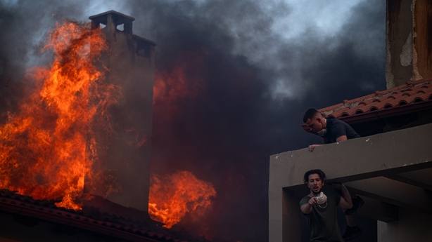 Local residents try to extinguish the fire of a burning house during a wildfire in Kryoneri, near Athens