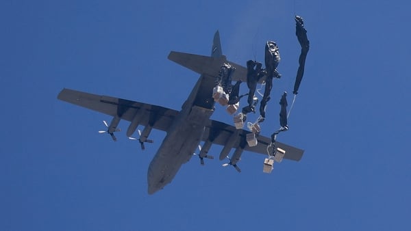A plane drops boxes of aid from a height with parachutes attached