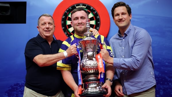 Luke Littler of England poses with The Phil Taylor Trophy alongside Garry Plummer, Owner of Target Darts and James Tattersall, Managing Director of Target Darts, after victory in the Final match between James Wade of England and Luke Littler of England on