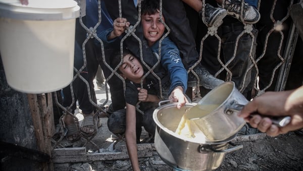 Two young boys are seen pressed against a metal fence holding pots trying to receive food in Gaza City