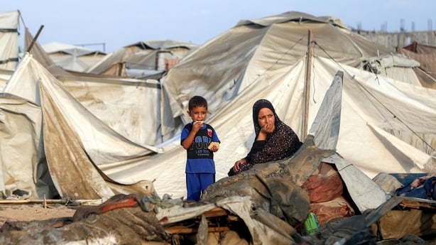 A woman and a boy sit by debris and destroyed tents following overnight Israeli bombardment at a camp in Gaza