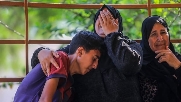 A teenage boy is held by a woman who is crying as another woman sites beside them in Khan Younis, Gaza