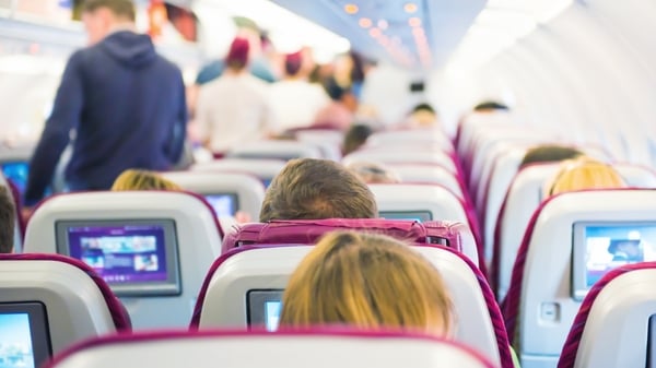Interior of airplane with passengers on seats waiting to take off and cabin crew in uniform walking the aisle