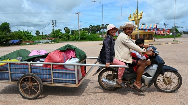 A woman, man and child are on a motorbike with a trailer behind it returning to their home on the Cambodia - Thailand border